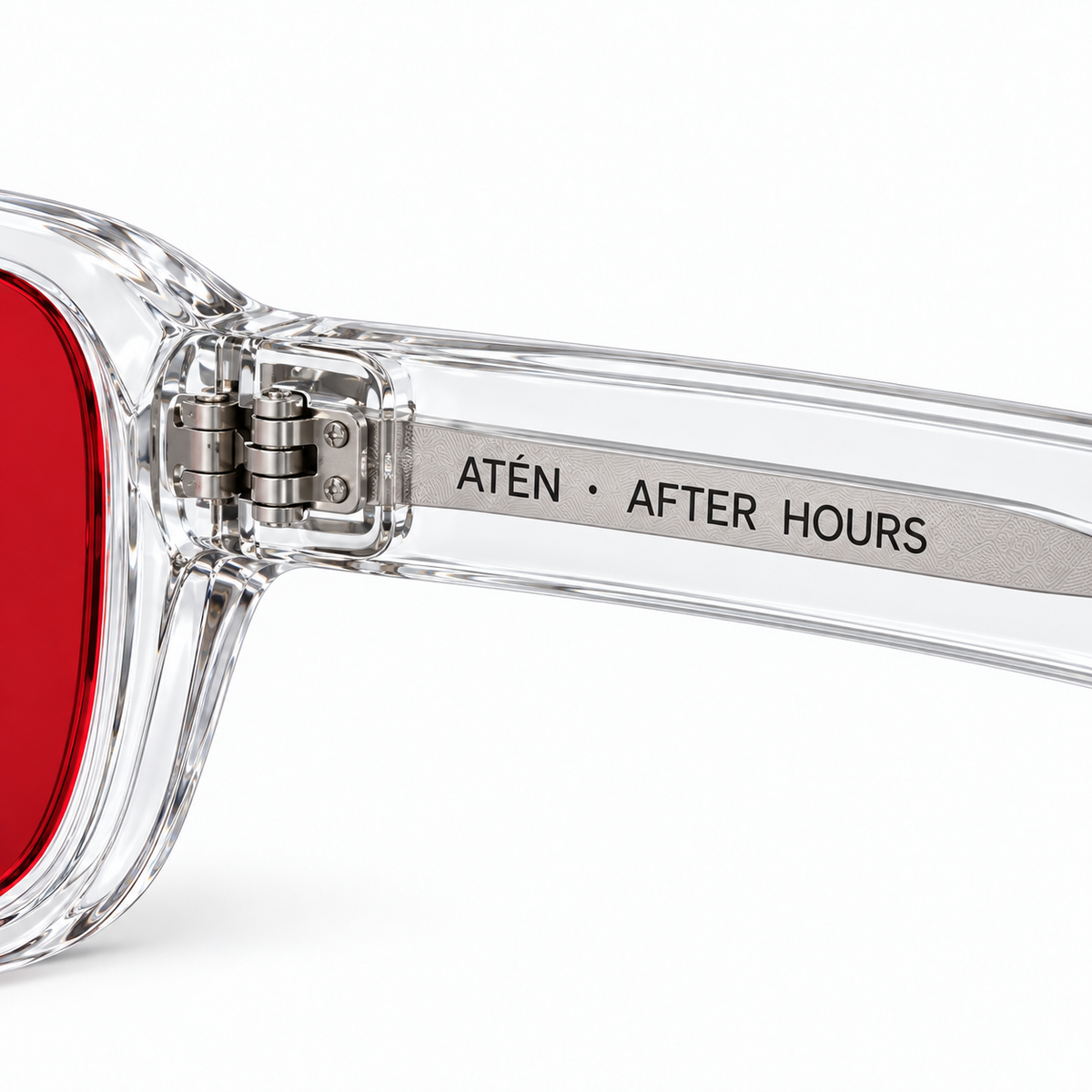 Macro of ATÉN Crystal Clear hinge, deep red After Hours lens edge and silver core reading “ATÉN · AFTER HOURS” on white background.
