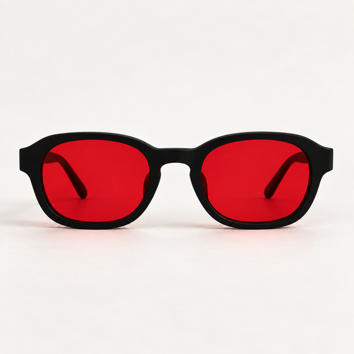 Front view of ATÉN Matte Black glasses with deep red After Hours lenses and both temple tips visible through the lenses on a warm ivory studio surface.