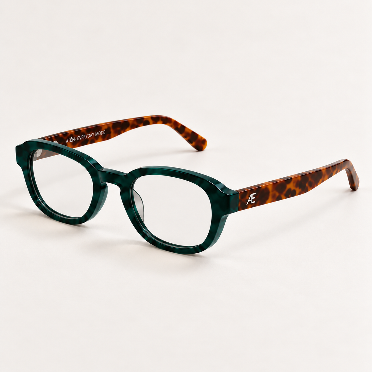 ATÉN Forest/Tortoise glasses with Everyday Mode lenses, three-quarter view on ivory; green front, brown temples and silver monogram.