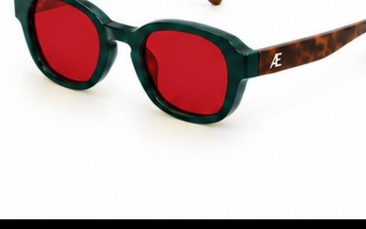 Open ATÉN Forest/Tortoise frame with deep red After Hours lenses in a cropped front-right three-quarter view; deep forest-green front, brown tortoiseshell temples and silver ATÉN monogram, on white with a thin black strip at the lower edge.