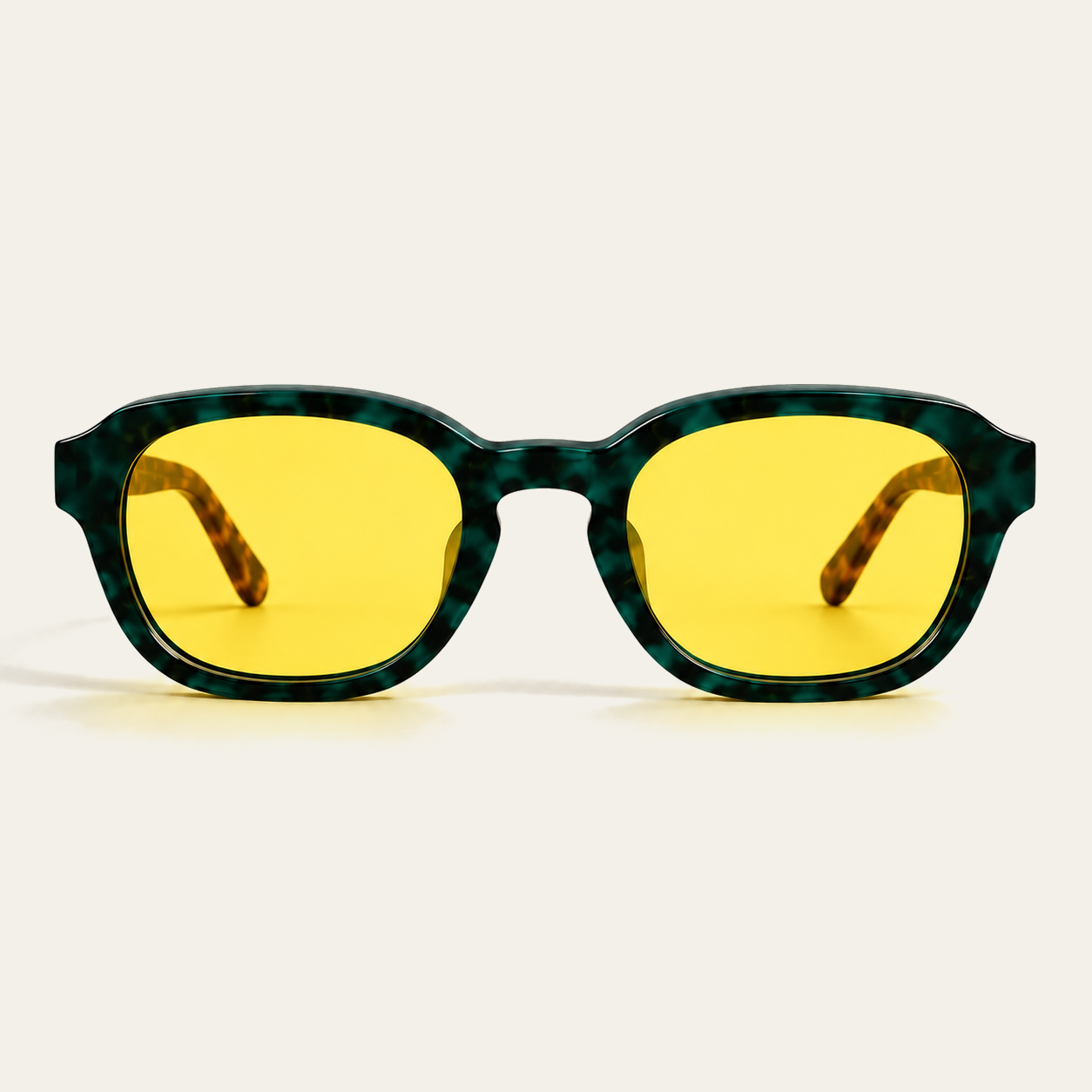 Straight-on front view of ATÉN Forest/Tortoise glasses with pronounced amber Focus Mode lenses; the deep forest-green marbled front is centred, brown tortoiseshell temple tips are visible through the pronounced amber lenses, and a soft amber-tinted shadow rests beneath the lower rims on the cream background.