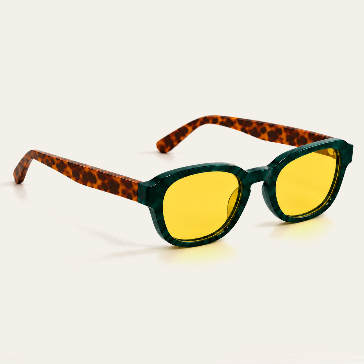 Rear three-quarter view of open ATÉN Forest/Tortoise glasses with pronounced amber Focus Mode lenses; the brown tortoiseshell temples cross behind the deep forest-green marbled frame, with warm pronounced amber lens reflections and a soft shadow on the cream background.